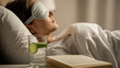 © Yulia - Woman relaxing in bed using a cooling eye mask, with a glass of cucumber water and an open book nearby, warm lighting and cozy atmosphere