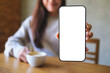 © Farknot Architect - Mockup image of a woman holding and showing a mobile phone with blank white screen while drinking coffee in cafe
