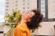 © Jose Calsina - A joyful young woman with beautiful curly hair experiencing a moment of pure happiness, smiling with her eyes closed, radiating positivity and carefree energy in an urban atmosphere.