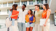 © Jose Calsina - A cheerful gathering of university students engaged in lively conversation while holding colorful folders, showcasing friendship and collaboration among diverse young individuals in a campus setting.