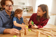 © Stockphotodirectors - A happy family spends the afternoon playing with wooden blocks and a train set on a sunny day. The parents guide their child as they build and create together.