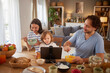 © Stockphotodirectors - Family members share a joyful breakfast, eating cereal and fruits while watching a show on a tablet. Their cozy living room is bright and inviting, filled with warm light.