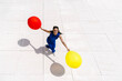 © VISTA by Westend61 - Woman in blue holding red and yellow balloons outdoors on bright floor