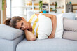 © Graphicroyalty - Sad woman lying on sofa with stomach pain holding pillow. Menstrual cramps, abdominal ache and loneliness concept. Young female suffering from period discomfort at home. Healthcare and medicine.