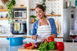 © Graphicroyalty - Happy woman in apron chopping fresh vegetables on wooden board in modern kitchen. Smiling female chef preparing healthy salad or soup. Vegan nutrition, organic food and wellness lifestyle concept.