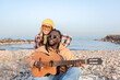 © Renata Hamuda - Happy multiracial couple enjoying music playing guitar on a rocky beach