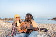 © Renata Hamuda - Happy multi-ethnic couple enjoying a day on pebble beach playing guitar