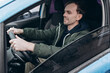 © MZaitsev - A young man looks intently at the road while holding onto the steering wheel while driving through the city.