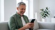 © Muhammad - Smiling Mature Man Using Smartphone on Gray Sofa in Bright Living Room