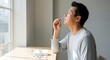 © QuiinL - Asian man performing a self-administered nasal swab test at home near a window.