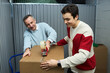 © DragonImages - Caucasian middle aged man and Caucasian teenager boy sealing cardboard box with packing tape dispenser in storage facility, both smiling and working together on moving or organizing belongings