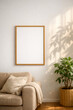 © You - Mockup of a blank vertical picture frame hanging on a white wall in a sunny living room with a beige sofa and leaf shadows