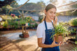 © we.bond.creations - Woman entrepreneur holding a potted plant and smiling while having a phone conversation in her greenhouse plant nursery