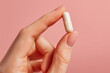 © Denis - Female hand holding pill capsule against vibrant pink background. Dietary supplements and healthy lifestyle.