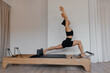 © Anton - Woman performs forward lunge and stretch on pilates reformer training machine