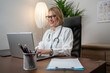 © Nenad - Woman physician working with AI medical assistant on laptop in clinic