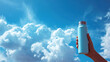 © DP - Hand holding a blue stainless steel water bottle against a bright blue sky filled with fluffy white clouds, symbolizing hydration and outdoor adventure