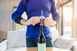 © Nimbus Works - Careful routine with senior man opening a wine bottle using a corkscrew, older male hands centered over wooden table in bright living room, everyday domestic action for lifestyle, leisure, home ritual
