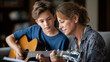 © Kateryna - Faceless music teacher and teenage student sitting on sofa learning to play guitar in private lesson in living room at home musical instruction domestic education with copy