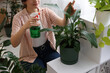 © New Africa - Woman spraying beautiful potted houseplant with water indoors, closeup