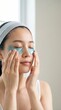 © Running opossum - young asian woman applying cooling eye patches in bright bathroom for skincare routine