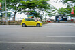 © Ardhiansyah - a yellow hatchback car driving on a road. The photo was taken using a panning technique, which keeps the moving car in focus while the background appears motion-blurred, giving a sense of speed