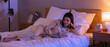 © Pixel-Shot - Beautiful young woman reading book and lying on bed in bedroom at night