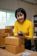 © Wasana - Asian woman entrepreneur checking orders on smartphone in warehouse, managing inventory