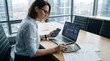© ibhonk - Focused businesswoman analyzing complex financial data using laptop, smartphone, and calculator in a brightly lit modern office boardroom.