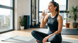 © Lisicus - Woman sitting on yoga mat in modern gym drinking water from bottle. Hydration and recovery after workout. Healthy fitness lifestyle and wellness concept