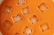 © los3amigos - Primer plano de cubitos de hielo flotando en un líquido anaranjado brillante.