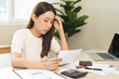 © KMPZZZ - Debt and financial concept, stressed asian young woman have a headache while female calculate expenses, income and expenses, looking bills of credit card for payment or payday on table at home office.