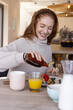 © wavebreak3 - Woman wearing sweater pouring syrup onto pancakes with berries at home dining table