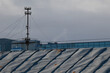 © k49red - A Simple Metal Support Structure Holding Electrical Wires And Insulators On A Standing Seam Roof. Urban Detail Against A Cloudy Sky.