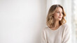 © Nataliia Pyzhova - Beautiful young woman with soft smile looking out the window, wearing light sweater, in bright room with minimal background