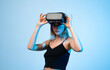 © Volodymyr_sh - Woman using virtual reality headset and hand gesture, immersive VR interaction concept with futuristic technology on blue background