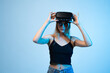© Volodymyr_sh - Woman adjusting virtual reality headset, modern VR technology and immersive digital experience concept on minimal blue background
