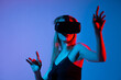 © Volodymyr_sh - Woman in VR headset reaching upward in virtual space, neon red blue lighting, immersive technology and gesture interaction