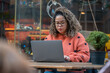 © lorenzophotoprojects - Brazilian woman remote working on laptop at outdoor cafe
