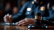 © Jayk - Judge's gavel on a wooden desk with a person in uniform writing in the background