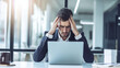 © zeen17 - Stressed businessman holding his head in frustration while looking at his laptop in an office setting, symbolizing work pressure and deadlines