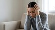 © HananElahi - Sad Young Woman Suffering from Headache and Depression Sitting on Sofa at Home Mental Health