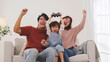 © eggeeggjiew - Happy Asian family celebrate victory during console gaming, raising hands and laughing together on the sofa.