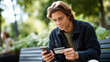 © Kateryna - Young man using smartphone and credit card outdoors in park mobile payment transaction in natural setting outdoor online shopping moment with technology casual digital banking