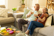 © Wavebreak Media - Diverse senior couple sitting on sofa in casual wear in living room, holding glasses, smartphone