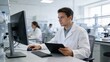 © Alexander - A scientist in a lab coat examines a tablet while seated at a desk with lab equipment. It conveys themes of research, innovation, and technological advancement in a scientific environment.