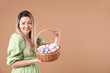 © New Africa - Easter celebration. Smiling woman in dress with wicker basket full of painted eggs on beige background, space for text