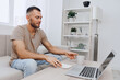 © SHOTPRIME STUDIO - Thoughtful man sitting on a couch, enjoying coffee while working on a laptop. A cozy home office atmosphere with a minimalist design, promoting productivity and comfort.