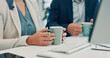 © SparkPix/peopleimages.com - Hands, business and woman in office with coffee, start day and planning for financial report. People, investor and professional in workplace for espresso, energy boost and pc for company audit or tea