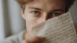 © CYBERPINK - Close-up portrait of a young man's face. he is holding a piece of paper in front of his face, covering his mouth with his hand. the paper appears to be a handwritten note or a letter.